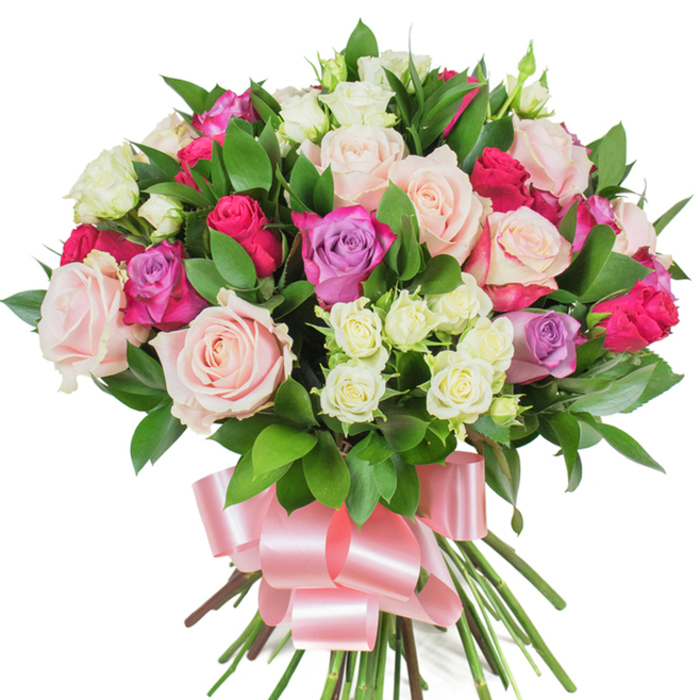 A sumptuous, garden-inspired bouquet of mixed roses presented against a pristine white backdrop, arranged with the precision and warmth of an Islington florist's hand. The visual centre is filled with large, fully opened roses in pale blush pink and creamy white - their ruffled layers forming soft, luminous cups - while brighter fuchsia or hot pink roses punctuate the scene with energetic colour. A sprinkling of lavender roses adds a cool, romantic counterpoint, lending subtle variation to the overall tonality. Interlaced among the main blooms are clusters of tiny spray roses in creamy white with soft yellow hints, which add scale contrast and delicate texture that catches the eye. Deep green, glossy foliage, likely ruscus or salal, is strategically placed to cradle the flowers and to emphasise the freshness of the petals; the elongated, shiny leaves create a rich backdrop that enhances the bouquet's three-dimensional fullness. The stems are bound together at the base and finished with a broad, baby pink satin ribbon tied into a generous bow, its smooth loops and trailing tails softening the composition and providing an elegantly feminine flourish. Against the white background, each petal, vein, and sheen is visible, suggesting a subtle rose fragrance and the tactile softness of newly cut blooms. This arrangement carries a celebratory, affectionate tone - ideal for birthdays, anniversaries, Mother's Day, or simply to brighten a flat near Mildmay Park or a quiet house on Newington Green - and it communicates genuine care through colour, texture, and classic floral craftsmanship.