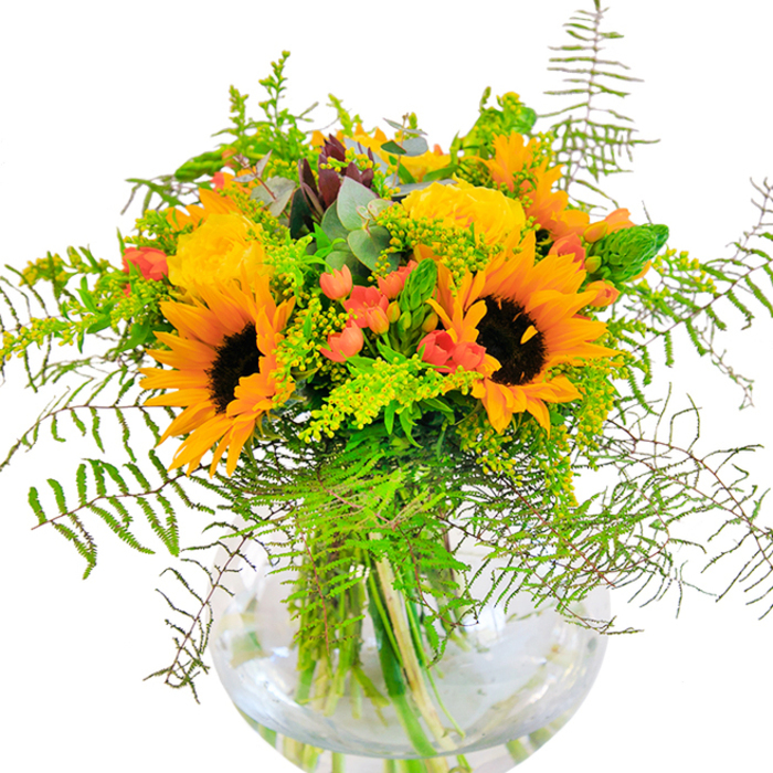 The bouquet captures the essence of late summer in Canonbury, glowing with golden sunlight and rustic abundance. Clusters of large sunflowers, their petals vivid yellow and centers deep brown, form the focal point-radiating warmth like the gardens around Canonbury's elegant terraces. Nestled among them, yellow garden roses spiral open, their smooth layers of petals bringing an old-fashioned charm. Scarlet Hypericum berries punctuate the bouquet, standing out like brilliant jewels amidst a lush tapestry of foliage. The greenery is a carefully balanced mix: airy ferns trail outwards with gentle motion, light green sprigs-likely solidago-bear cheerful mini blossoms, while slender spikes and cool eucalyptus leaves introduce both height and contrast. Seated in a clear, spherical glass vase, every stem is on display, creating a sense of openness and vitality that mirrors Canonbury's tranquil, cosmopolitan atmosphere. From up close, you'd sense the textures shifting under your fingertips-velvety sunflower faces, droplets of berry gloss, and the crisp snap of just-cut greens. The bouquet's fragrance is as inviting as an open garden gate after rain. Ideal as a centerpiece for milestone occasions, housewarmings, or even a spontaneous gesture of care, this arrangement speaks to the shared happiness at the heart of Canonbury life-a floral story artfully written with every petal.