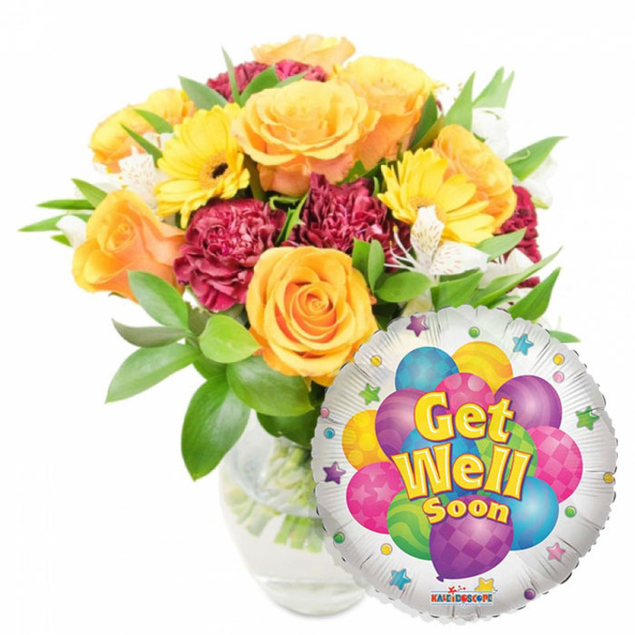This bright Get Well Soon gift reads as a conversation in colour and texture, carefully assembled in a clear glass vase with stems visible through the water. At its centre, several large roses in soft orange and deep golden-yellow open in layered spirals, their velvety petals offering a gentle citrus nuance that mingles with the cool freshness of green leaves. Yellow gerbera daisies punctuate the bouquet with bold, sunny faces that lift the mood, while deep maroon carnations tuck in among them to provide ruffled density and a rich tonal counterpoint. Sprays of white alstroemeria punctuate the arrangement like lunar touches, their delicate petals and subtle markings adding lightness and air. The foliage is abundant-glossy, varied and cradling each bloom so the overall silhouette feels generous and garden-inspired. Positioned toward the lower right and slightly overlapping the flowers, a metallic silver Mylar balloon adds a playful, reflective note. Its central graphic is a cheerful cluster of cartoon balloons in bright pink, sky blue, lime green, purple and yellow, some patterned with polka dots and stripes, and bold yellow-and-blue lettering announces Get Well Soon across the face. Small colorful starbursts dot the balloon's white rim and a tiny KALEIDOSCOPE logo is visible along the bottom edge. Bathed in diffuse studio light, this pairing of flowers and balloon conveys warm encouragement and tender care-an ideal pick-me-up delivered locally across Canonbury toward Upper Street, Canonbury Square or Islington's quieter streets when someone needs a bright lift during recovery.