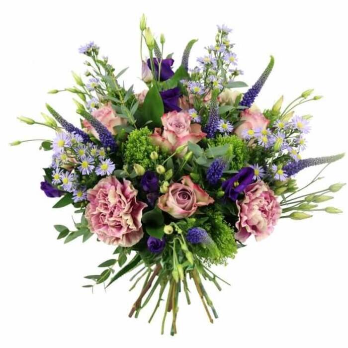 Set against a clear white background, a beautifully rounded, hand-tied bouquet overflows with pink, mauve, and purple blooms, the kind of carefully balanced arrangement often seen in Canonbury's elegant townhouses. The central focus is on an assortment of roses in soft pastel pinks, some still held in tight buds and others spreading wide into open rosettes, their petals layered in gentle spirals and shifting from deeper pink in the core to paler, almost ivory-tinted edges. Interwoven among them are large carnations in dusky rose and purple-mauve tones, their densely frilled petals adding volume and a tactile, almost billowing texture. Standing proud amidst this softness, slender spikes of deep lavender-blue Veronica lift the eye upward, giving the design a vertical rhythm and a slightly whimsical, garden-border feel. Nestled between the larger flowers are clusters of rich purple lisianthus, their bell-shaped blossoms and softly curling buds offering contrast and depth. Scattered throughout the bouquet, tiny daisy-like flowers in light lavender and periwinkle with soft centres create a misty, cloud-like veil, filling spaces and lending an airy delicacy. Surrounding all the blooms, layers of foliage in varied greens frame the colours: cool, silvery eucalyptus leaves, brighter lime-green filler, and deeper green stems weave together to provide structure, freshness, and natural movement. At the base, the stems are gathered into a tight, clean hand-tied bundle, cut evenly and clearly visible, ready for placing into a vase on a Canonbury windowsill overlooking the quiet residential streets. This bouquet evokes a sense of refined celebration and heartfelt warmth, ideal for anniversaries, milestone birthdays, or thoughtful flower delivery to homes and studios tucked between Islington's boutiques and the calm of Canonbury's garden squares.