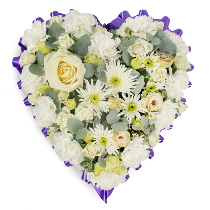 Struck in a classic heart silhouette, this memorial piece is densely populated with soft white and cream blooms that create a refined field of texture. The eye is drawn first to a large, perfectly formed creamy-white rose at the centre, its petals arranged in a tight, elegant spiral. Radiating outward, the arrangement alternates soft ruffled carnations and compact spray chrysanthemums with longer, spidery chrysanthemum petals that add a subtle spiky rhythm across the surface. Interspersed cream rosebuds and small lisianthus clusters bring pockets of delicate form and understated colour variation-touches of pale yellow and almost-peach at the bud edges-while tiny lime-green button-like buds provide fresh punctuation. Cool-toned eucalyptus foliage, with its silvery-blue cast, is strategically tucked between blossoms to give depth, natural movement and a faint, herbal aroma that complements the floral perfume. The heart's perimeter is crisply defined by a rich purple, pleated ribbon border, scalloped to create a formal frame that honours the arrangement's commemorative purpose. The overall composition suggests meticulous hand-crafting: careful massing near the centre that gradually softens toward the curved edges, a balance of volume and delicate detail intended to express dignity, peace and abiding affection. As a Canonbury-style tribute, it suits memorial services in local churches or funeral homes near Essex Road and Canonbury Road, prepared for attentive local delivery and placement.