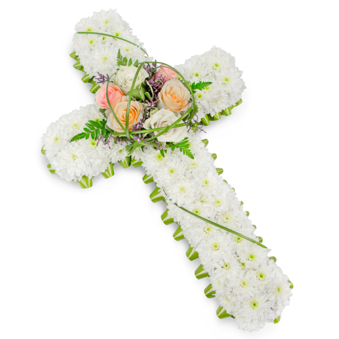 A beautifully crafted floral cross is displayed on a bright white background, its calm elegance evoking the gentle, reflective mood of a quiet morning in Canonbury. The cross is formed from a tightly packed bed of small white chrysanthemums or similar delicate blooms, each flower carefully placed so that no spaces are visible, resulting in a soft, plush texture that seems almost cloud-like. This unbroken expanse of crisp white speaks of purity, serenity, and a respectful farewell. Running continuously around the outer edge of the cross is a slim, bright green border, likely made of fresh foliage or closely trimmed greenery. This vivid green band outlines the shape with precision, adding contrast and structure in much the same way the mature trees frame the peaceful paths near Canonbury Station. At the meeting point of the vertical and horizontal arms, a slightly raised cluster of feature flowers forms a gentle focal point. Several roses in warm, comforting shades-creamy ivory, soft blush pink, and mellow peach-are arranged so their layered petals open towards the viewer, bringing warmth and human tenderness to the design. Intertwined among the roses are airy fern fronds, sprigs of leafy greenery, and slender blades of bright green grass arcing with natural movement. Small spikes or clusters of tiny purple filler flowers add a discreet hint of colour, deepening the visual interest without disturbing the calm. The overall effect is one of balanced proportion and thoughtful craftsmanship, with each element chosen and placed to convey love, faith, and remembrance. This floral cross would be fitting for a church in the Canonbury area, a crematorium service, or a graveside tribute, offering a dignified expression of sympathy and enduring connection to the departed.