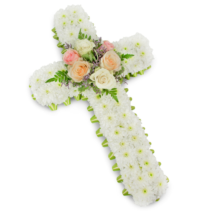 A beautifully composed funeral flower cross is displayed on a clean white background, reminiscent of the peaceful interiors of Canonbury's small churches and chapels. The cross follows a classic Latin shape, its vertical and horizontal arms filled from edge to edge with tiny white button chrysanthemums. Each bloom is placed closely against the next so that the entire surface appears like a continuous blanket of white, slightly domed and soft-looking, as though it would give under a gentle touch. The individual petals form intricate textures that catch the light, conveying a feeling of innocence, serenity, and enduring remembrance. Along the perimeter of the cross, a lime green ribbon wraps neatly around the structure. It peeks out just beyond the mass of white petals, forming a narrow frame that sharpens the silhouette and introduces a fresh, natural contrast. This subtle edge of green recalls the spring foliage along Canonbury's quiet residential streets, offering a hint of renewal amid grief. At the crossing point of the arms, a small but striking bouquet forms the centrepiece. Here, several roses in varying pastel shades-soft blush pink, delicate peach, and creamy white-are fully open, their layered petals unfurling in gentle spirals. Fine sprigs of light purple or lavender filler flowers and airy green fern fronds weave among the roses, bringing movement and depth to the central cluster. The colours remain muted and respectful, ideal for a church funeral, memorial service, or graveside tribute. This floral cross, carefully arranged with a focus on balance and proportion, would be a meaningful choice for families in Canonbury and nearby Highbury seeking a symbol of faith and a loving final message. The entire design radiates calm, making it a comforting presence during a time of loss.