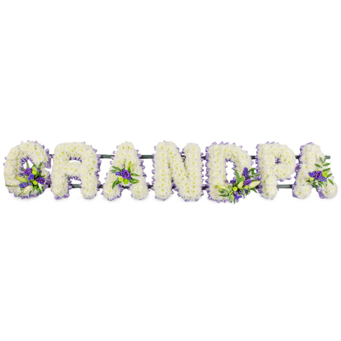 Displayed against a plain white backdrop, this bespoke funeral flower arrangement spells out the word GRANDPA in broad, block-style capital letters, each one generously filled with fresh, snow-white blooms. The letters sit in a neat horizontal line, evoking stability and calm, as if ready to be placed in front of a coffin or on trestles at a Canonbury church or chapel. Close inspection reveals hundreds of small white chrysanthemums or carnations closely nestled side by side, their petals overlapping to create a plush, continuous blanket of texture. The flowers are so densely packed that they form rounded, sculptural shapes, giving each letter a soft yet clearly defined outline. Carefully woven into this white base are accents of deep purple and lavender flowers, accompanied by short stems of green foliage. These coloured clusters are positioned with intention: a vibrant group anchored at the curve of the G, others glowing from the hollows of the As, and additional highlights brightening the D and P, offering a gentle contrast that draws the eye without overwhelming the serenity of the design. Beneath the blossoms, a dark green metal or plastic bar links the letters together, mostly hidden but essential for carrying and displaying the tribute at a service in Canonbury, nearby Highbury, or along the Regent's Canal. The overall mood is one of quiet reverence and personal remembrance, the sort of custom-made piece Canonbury Flowers might create to help a family honour their grandfather's life-an arrangement that speaks of enduring love, shared history, and the wish to say goodbye with grace and beauty.