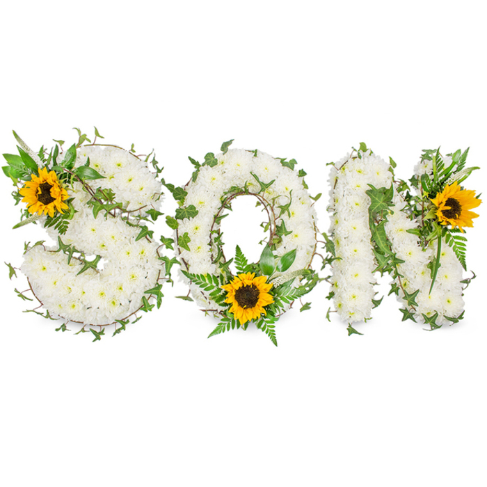 This image shows a carefully constructed sympathy tribute spelling out the word SON in uppercase letters, arranged horizontally against a pure white background. Each letter is robustly built from hundreds of small, pristine white chrysanthemums, packed densely so the letterforms read as soft, sculpted blocks of floral texture. Winding through the white chrysanthemums are sprigs of dark green ivy, their pointed, lobed leaves and trailing stems threaded through the design to add depth and a natural, evergreen accent. Complementing the white and green palette are three striking sunflowers, placed deliberately as focal accents: a large sunflower adorns the upper-left curve of the S, a second sunflower nestles at the lower center of the O among feathery fern fronds and narrow, pointed leaves, and a third flower is set on the upper-right shoulder of the N. Each sunflower shows broad, golden-yellow petals radiating from a prominent dark brown centre, introducing warmth and a sense of life to the composition. Studio lighting from above creates soft highlights on the chrysanthemums and subtle shadows beneath the foliage, revealing the three-dimensional construction and meticulous florist technique. The arrangement reads as both a personalised memorial for a son and as an example of formal funeral floristry often requested by families in Canonbury, Canonbury Square and along Essex Road. Texturally rich, visually clear and composed with respectful restraint, the piece balances purity, remembrance and gentle optimism.