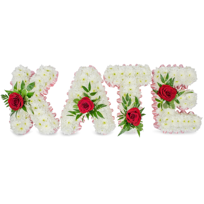 A dignified, personalised floral tribute spells out KATE in bold capital letters, each letter formed from a thick, voluminous mass of crisp white chrysanthemums that give the surface a soft, quilted appearance. The letters stand out against a stark white background, allowing the texture of the tiny chrysanthemum petals to read clearly and calmly. Around every letter's contour a slim, pale pink satin ribbon has been applied like a lace of colour, softening the edges and introducing a gentle contrast that feels refined rather than showy. At the centre of each letter, a single deep red rose provides a poignant focal point-rich, velvety petals that catch the eye and convey affection. Those roses are surrounded by abundant greenery - broad, glossy leaves and feathery fern fronds - which add sculptural depth and a natural frame to the roses. The florist has placed the roses with careful balance: on the K the rose and foliage sit low on the left vertical stroke; the A is crowned with its rose at the peak of the triangle; the T's red bloom is placed at the base of the left side of its crossbar; and the E's rose nestles on the middle horizontal arm. This arrangement carries the quiet, respectful tone of a memorial piece for funeral or celebration-of-life services, meant to express love, purity and remembrance. As a Canonbury-based design I picture it arriving in the calm light of a chapel near Canonbury Square, offering simple, heartfelt beauty to family and friends.