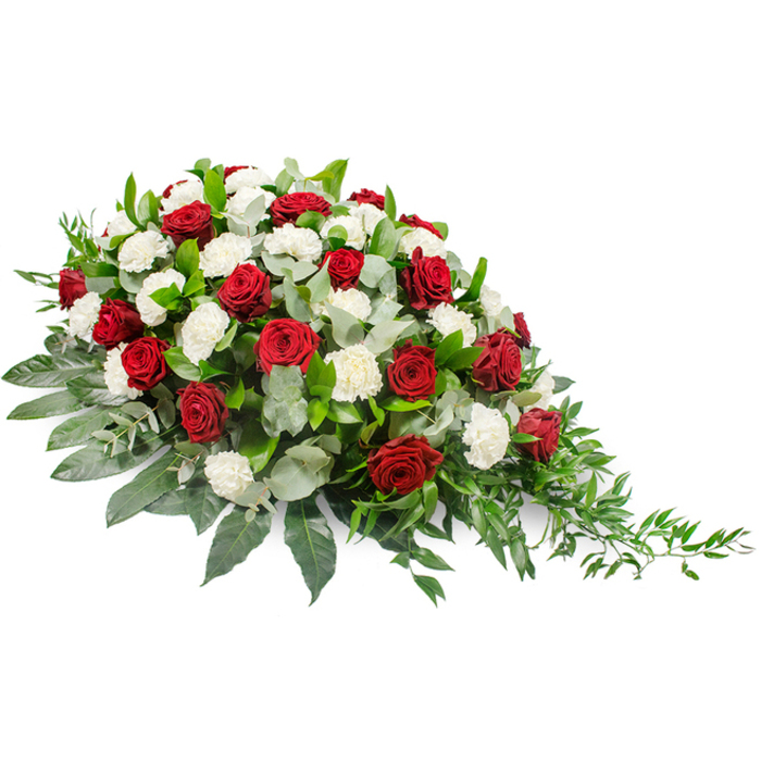 A refined funeral flower spray in traditional red and white is set against a bright white backdrop, so that every petal, leaf, and curve is clearly defined. The arrangement is elongated and horizontal, fuller and more substantial on the left side and narrowing as it sweeps toward a delicate, pointed tip on the right, creating a soft crescent shape. Rich crimson roses stand out immediately, their tightly layered petals forming luxurious, cup-shaped blooms that suggest deep affection and solemn respect. Nestled between them are numerous white carnations, their ruffled petals forming cloud-like clusters that lend lightness and a sense of gentle purity. The interplay of the deep red and brilliant white blooms creates a striking yet comforting contrast, a visual metaphor for grief and peace existing side by side. Beneath and around the flowers lies a generous layer of greenery: broad, dark leaves give the spray a strong structure and frame the blooms, while sprigs of silvery-green eucalyptus are tucked throughout, adding both texture and a muted, smoky tone to the composition. Along the right-hand side, trailing sprigs of lighter green foliage extend beyond the body of the arrangement, adding movement, softness, and a touch of natural wildness. The spray feels considered and composed, as if prepared by an experienced Canonbury florist familiar with local families' preferences for understated elegance during times of loss. It is easy to imagine this piece resting on a casket at a quiet service near Canonbury Square, or carried into a chapel as a final tribute, its colours and shapes conveying love, remembrance, and a respectful farewell.