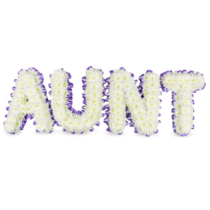 A meticulously arranged sympathy piece spells the word 'AUNT' in bold, gallery-sized letters, each formed by a dense carpet of small, immaculate white spray chrysanthemums. The multitude of tiny petals creates a soft, tactile surface that reads as both delicate and enduring; flecks of pale yellow at the flower centres add a subtle, natural warmth that prevents the composition from feeling austere. Each letter is outlined in a deep purple satin ribbon, carefully ruffled and pleated to provide a textured frame that accentuates the letter shapes and adds a note of refined contrast against the white blooms. Soft grey shadows beneath the letters emphasise their relief from the white ground, suggesting a solid, tasteful construction that will hold up during viewing at a service. The scent is mild and green, like washed linen, reinforcing the arrangement's serene mood rather than dominating it.  As an Islington-made tribute, this piece carries the quiet authority of a florist who understands local customs-from small chapel services near New River Walk to larger gatherings on Upper Street. The white chrysanthemums are chosen for their longevity and association with remembrance, while the purple edging introduces a dignified, almost poetic cadence to the composition. Placed near Canonbury Square or delivered along Essex Road, the tribute functions both as a clear, personalised message and as a comforting focal point for family and friends to gather around in memory of a treasured aunt.