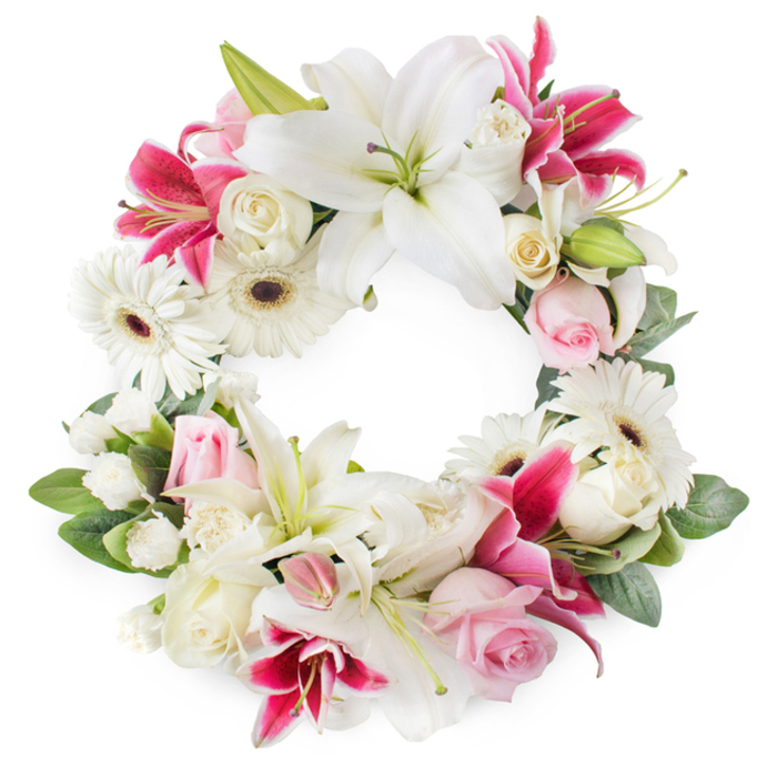 Captured against a simple white backdrop, this elegant heart-shaped funeral wreath forms a hollow centre, its outline traced by a lavish mix of white, soft pink, and deep magenta blooms arranged with the care of an experienced Canonbury florist. The heart is defined by large white Oriental lilies, their petals broad and smooth like satin, opening wide to reveal soft green throats and golden stamens that seem to glow in the gentle light. Weaving between them are striking deep pink and fuchsia lilies, with star-like forms and subtle speckling, adding warmth and depth to the design while preserving its solemn beauty. Tucked closely around the lilies are clusters of roses in delicate blush and creamy white; some are fully open, showing their layered, spiralling centres, while others remain in bud, symbolising memories still treasured and love that continues quietly. White gerbera daisies, with their dark, clearly defined centres and neat, radiating petals, offer contemporary contrast and a sense of calm clarity, like the peaceful corners of nearby Canonbury Square. Between the larger flowers, tiny white filler blooms, likely miniature carnations or spray chrysanthemums, create soft clouds of texture, ensuring there are no gaps and giving the wreath a rich, cushioned appearance. A frame of lush green foliage, with leaves in various shapes and tones, supports the heart shape and adds natural movement, as though the flowers have just been gathered. The overall impression is one of compassion and respect, making this heart wreath fitting for images accompanying articles on sympathy flowers, funeral tributes, or celebrations of life held in Canonbury churches and crematoriums across Islington, where families seek a tender and dignified floral expression of farewell.