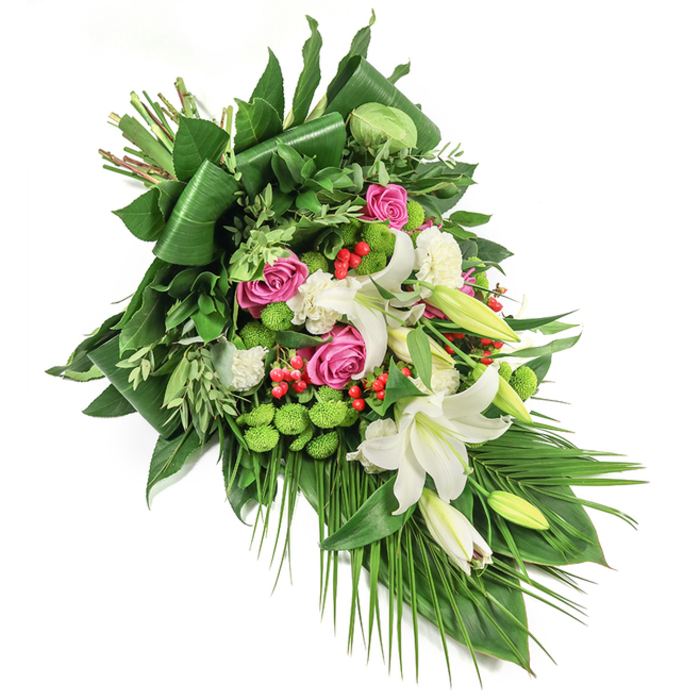 Presented diagonally on a flawless white background, this grand and elongated funeral spray reflects the careful artistry of Canonbury's local florists. The composition stretches from the top left to the bottom right, capturing the eye with its rich interplay of form and colour-much like the varied landscapes that thread through the gardens of Canonbury. The focal point, several majestic white oriental lilies, command attention with their broad, fragrant petals and bright golden-yellow stamens, some blooms unfurling wide while others remain in promise-filled bud. Clusters of deep pink roses, ranging from tight buds to lush, open blossoms, are thoughtfully woven throughout, adding warmth and the sentiment of remembrance. Textural interest blossoms from patches of ruffled white carnations and the rounded, lively green of button chrysanthemums, whose mossy texture is reminiscent of Canonbury's hidden lawns. Brilliant red hypericum berries pop against the dominant greens and creamy whites, strategically dotted amidst a backdrop of glossy aspidistra, feathery ruscus, and delicately curved palm fronds that trail in graceful sweeps. The lush, abundant foliage both structures and softens, grounding the arrangement in its local context and infusing it with a sense of calm and respect. This dignified spray is a classic choice for expressing sympathy and memorialising loved ones in Canonbury, its premium blooms and fresh greenery a testament to the area's gentle spirit and the florists' commitment to heartfelt, local craftsmanship.