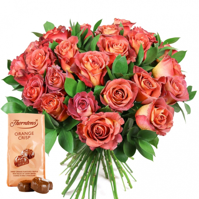 A luxuriant arrangement of open roses commands the scene, their tightly packed, rounded form displaying the kind of precise hand-tying found in Canonbury's best independent flower studios. Warm peach, soft coral, rose pink, and deeper salmon tones blend seamlessly on each bloom, with delicate bicolour gradients and ombre effects creating a tapestry of warmth. Pale yellow and cream nestled at the centre of select roses add light and interest, echoing the sun-dappled ambiance of summer afternoons spent at Canonbury Square. The foliage - abundant, dark green, and polished - threads between the flowers, reminiscent of the lush tree canopies seen throughout local parks. The bouquet sits against a clear, fresh white background, which amplifies every shade and petal's subtle shadow. Positioned thoughtfully in the lower left is a rectangular Thorntons Orange Crisp chocolate pouch, easily recognisable by its light beige wrapping, the 'Thorntons' logo at the top, and ORANGE CRISP in prominent, dark print. An illustration just beneath teases the truffle's contents: tangy orange cream encased in crispy, milk chocolate shells. Directly ahead, two real, glossy chocolate truffles rest temptingly. The bouquet's clean, trimmed stems extend beneath the flowers, alluding to their just-picked freshness and the expert touch of Canonbury Flowers. This image captures the essence of modern gifting in North London - a glowing, tactile arrangement ideal for anniversaries, birthdays, or simply letting someone know they are cherished.