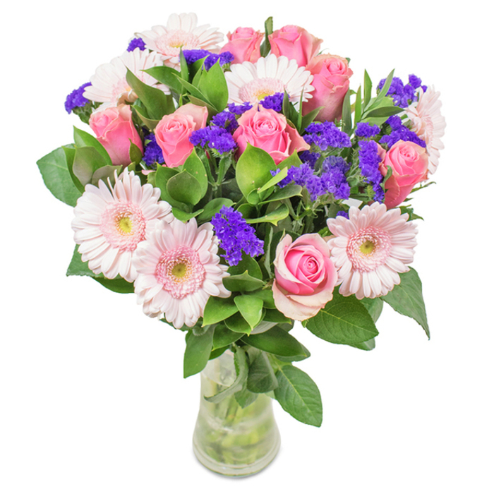 An elegant bouquet stands out against a pristine white backdrop, authentically arranged by Canonbury Flowers near the heart of north London. About seven to nine pink roses-some in bud, others opening in perfect spirals-give a sense of continuity, romance, and grace. Surrounding them are five to seven pale pink gerbera daisies, their large, round faces and soft, nearly white centres capturing gentle natural light like blooms in nearby Highbury Fields. Threaded throughout are clusters of vivid purple statice, bringing a pop of texture and deeper colour that makes the pinks and blushes shimmer with vitality. Generous deep green foliage, lush and glossy, frames every bloom, conjuring the freshness of local gardens along Canonbury Road. The clear glass vase showcases stems and water, reinforcing the bouquet's honest, natural beauty-a hallmark of fresh flower delivery from local artisans. Designed with special occasions in mind-whether a joyful birthday, an anniversary dinner, or a thoughtful gift for a friend along Essex Road-this arrangement radiates celebration, affection, and the unique charm of Canonbury.