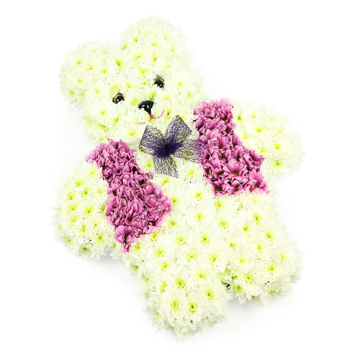 This image shows a meticulously crafted floral teddy bear tribute, the kind a Canonbury family might choose for a deeply personal farewell or a christening celebration. The teddy is entirely made from white and creamy chrysanthemums, tightly clustered to form a rounded, cuddly silhouette. Each bloom contributes to the plush impression of the bear's head, snout, ears, tummy, and legs, with the petals creating soft ripples that catch the light like gentle fur. The face is expressive but understated: small, glossy, dark eyes are set into the cushion of petals, giving a look of calm, almost watchful kindness, while a neat black triangular nose sits just above a suggestion of a smile, achieved through careful positioning of petals or subtle pink detailing. Across the front of the bear, a waistcoat of rich pink and magenta flowers has been thoughtfully placed, with each side shaped like a little lapel, reminiscent of a child dressed up for a special day in one of Canonbury's churches or chapels. At the neckline, a delicate violet or deep purple net bow softens the transition between the pale body and the bold vest, adding an extra note of care and personality. The entire arrangement rests against a clear white background, free from distractions, allowing the craftsmanship and tenderness of the design to stand out. It's easy to imagine this floral bear bringing solace to a family gathering near Canonbury Square or Highbury Corner, where it can act as a floral embrace-honouring a child's memory, celebrating a new life, or offering gentle comfort in times of loss.