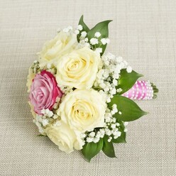 Imagine a serene Canonbury afternoon, where a small, elegant bouquet rests at a graceful angle atop light, textured linen reminiscent of local artisan markets. At its heart, creamy-white roses open luxuriously, their velvety petals swirling outward, symbolising purity and celebration. Among them, a striking magenta-pink rose glows vibrantly, adding dramatic flair much like the vibrant blooms seen at Newington Green in spring. Wisps of white baby's breath meander throughout, their airy blossoms bringing softness and movement, as deep green foliage anchors the bouquet with richness akin to the leafy canopies of Canonbury Square. The stems, tightly held in a brilliant pink satin ribbon, are further embellished by a delicate twist of pearls, catching the light in subtle, sophisticated sparkles. The bouquet radiates quiet romance and heartfelt joy-just right for a wedding in a local church or a joyful celebration on nearby Alwyne Road. With each detail-colour, shape, and shimmer-this arrangement reflects the skilled touch of Canonbury Flowers and the timeless atmosphere of North London, inviting memories of sunlit celebrations and new beginnings close to home.