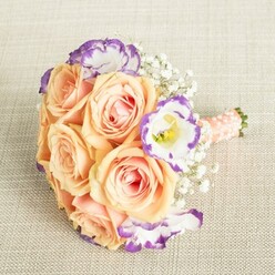 Light spills across a sumptuously hand-tied bouquet, its palette echoing the warm, welcoming architecture of Canonbury streets. Soft peach and apricot roses, their petals like brushed silk and dappled with pale pink, form the lush heart of the piece, embracing the promise of new beginnings. Amid the roses, crisp white Lisianthus blooms with ruffled, violet-tinged edges leap out-delicate but striking, adding an unexpected flash of artistry, much like the vibrant gardens of New River Walk. Clusters of ethereal Baby's Breath beam with quiet tradition, weaving through the design like wisps of pure joy. The stems, bound tightly in smooth peach satin and finished with a row of tiny pearl beads, suggest care and local craftsmanship-a signature touch from Canonbury Flowers. This bouquet feels perfect for a bride in St Mary's Church, for a bridesmaid, or to adorn treasured gatherings, imbuing any Canonbury celebration with grace, fresh fragrance, and the quiet reassurance of flowers prepared from the heart.