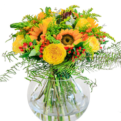 A glorious floral arrangement bursts forth in a clear, round vase, embodying the warmth and vitality of Canonbury's vibrant character. Dominating the composition are radiant sunflowers, their golden-yellow petals and dark, textured centers directed outward as if to soak up imaginary sunshine flooding a north London window. They are joined by spirals of buttery-yellow roses, their plush petals curling gently inwards, exuding softness and refinement. Lively red Hypericum berries glitter among the blooms, lending a playful accent much like the spirited colours found near Highbury Fields in autumn. The greenery offers a gentle embrace-wispy fern fronds arch with delicacy, mixed with sprigs of goldenrod dusted with tiny yellow flowers and slender, upright spikes. Hidden throughout are the silvery-green discs of eucalyptus, weaving a subtle fragrance that conjures woodland walks in Canonbury's nearby parks. The vase's clear glass reveals the stems' elegant intersection, grounding the bouquet in a sense of clarity and balance. Standing close, the bouquet's scent is uplifting yet nuanced: rose, fresh earth, and the lightest hint of wildflower honey. This arrangement instills a spirit of togetherness and celebration-perfect for commemorating a birthday, offering comfort, or simply bringing a joyful glow into a Canonbury living room, with same-day freshness from a local florist who knows the area's style and rhythm.