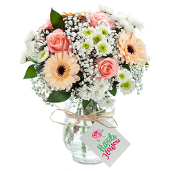 Picture the gentle calm of Canonbury mornings, where sunlight streams across tranquil Islington terraces-this serene mood is captured by a masterfully arranged bouquet depicting pure affection and artistry. At the centre, classic roses in delicate tones of peach and soft pink spiral serenely open, their fragrance subtle yet inviting. Two prominent, sunlit peach gerbera daisies sit with cheerful poise, their immaculate petals fanning around striking dark centres. Woven throughout are clouds of white baby's breath, infusing a sense of airiness and gentle whimsy, while crisp white spray chrysanthemums glimmer, their green-limed hearts peeking out and evoking the freshness of a walk through Highbury Fields in spring. Sparse stems of eucalyptus and glossy, deep green foliage provide a natural, lively contrast, their texture echoing the heritage plane trees of Canonbury's streets. The stems are gathered in a clear, textured glass vase, sturdy and classic, revealing the crisp cut flowers immersed in clean water. A rustic strand of raffia is looped around the vase's neck, tied delicately, with a white tag suspended as an invitation for a heartfelt message. This bouquet, available for same-day delivery from local florists, evokes a sensation of warmth and renewal-ideal for days of celebration, gentle encouragement, or simply to bring the soothing elegance of Canonbury's gardens into one's home.