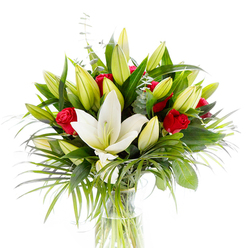 A refined floral composition centred on a single, large creamy-white Oriental lily in full bloom - its satiny petals slightly curved outward to reveal pale yellow stamens and a soft green pistil - dominates this bouquet with quiet elegance. Surrounding it, clusters of lime-green and pale yellow lily buds in various stages of opening add energy and optimism, while small, velvety red rosebuds peek through the foliage like secret notes of passion. The arrangement is grounded by glossy, deep forest-green leaves that give structure, and enlivened by longer, feathery palm fronds in a brighter emerald tone that arc and spill with graceful movement. Cool, rounded eucalyptus leaves in a silvery-green provide subtle contrast and texture, their matte surface refracting light differently from the glossy leaves. Everything is presented in a clear, cylindrical glass vase, the stems visible beneath the water line, lending a clean, modern honesty to the design. Photographed on a stark white background, the colours read vividly: the lily's purity, the rose's intensity, and the layered greens. The scent suggested is a blend of the lily's powdery sweetness and the rose's warm richness, creating an intimate, celebratory mood. Crafted with local care and familiarity with Canonbury's neighbourhood rhythms - from Canonbury Square to Essex Road markets - this bouquet reflects the careful hand of a local florist and is suitable for occasions ranging from anniversaries to thoughtful congratulations. Canonbury Flowers prepares arrangements like this with attention to freshness and composition, and they are available for delivery across the Canonbury and Islington area when requested.