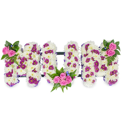 This personalised sympathy piece spells MUM in three bold, sculptural letters, each densely formed from pristine white chrysanthemums that create a thick, velvety surface reminiscent of fresh snowfall. Interwoven among the white are small pockets of rich magenta and purple spray blooms that give depth and a gentle visual cadence across the letters. Bright pink spray roses punctuate the design-two to three roses cluster at the top left of the first M, a larger spray of four to five roses nestles within the lower curve of the U, and a matching cluster crowns the top right of the final M-each grouping cushioned by deep green ferns and mixed foliage. Tiny blue accent flowers appear like shy stars against the white, pulling the eye to the carefully considered placements. A slim dark rail links the three letters horizontally, offering discreet support, while a thin purple ribbon subtly outlines the shapes and enhances their clean geometry. The overall mood is one of tender respect: the tactile chrysanthemum base suggests permanence and purity, the pink roses read as intimate tokens of love, and the darker tones add solemnity without gloom. Imagined here under the soft, cool light of a Canonbury chapel or arranged in a quiet corner near Canonbury Square, the tribute feels rooted in local sensibility-thoughtful, understated and expertly made. For families seeking a meaningful floral message, this arrangement communicates devotion and remembrance with careful floral craftsmanship and understated elegance.