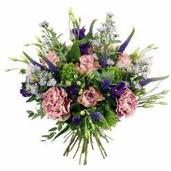 A lush, dome-shaped bouquet of pink and purple flowers is captured in crisp detail against a white backdrop, showcasing the kind of artistry you might expect from a seasoned Canonbury florist. At a glance, the eye is drawn to the roses: soft pastel pink blooms layered with petals that curl gently outward, some fully open and others just beginning to unfurl, revealing warmer blush tones at their centres. Interlaced with these are generous carnations in muted mauve and dusty rose, their densely ruffled petals creating a cloud-like texture that feels both cosy and refined. Rising gracefully above the rounded mass of blossoms, slim spikes of deep indigo Veronica provide vertical lines and a slightly wild, garden-grown character, reminiscent of the borders along nearby Canonbury Square. Rich purple lisianthus blooms, some open and some still in bud, add velvety depth, while sprays of tiny lavender and periwinkle aster-like flowers scatter delicately throughout, softening every edge with their star-shaped petals. Around the blooms, a mix of fresh foliage brings the arrangement to life: bright, lime-green textural filler sits alongside muted sage-green eucalyptus and other glossy leaves, creating a pleasing play of tones from chartreuse to deep forest green. The stems are gathered neatly in a classic hand-tied finish, their cut ends aligned and visible beneath the blossoms, ready to drop into a vase on a Canonbury kitchen table or office desk near Essex Road. This bouquet feels like a modern classic-perfect for celebrating a birthday, sending a romantic gesture, or simply bringing a burst of colour and fragrance into a home overlooking the leafy streets around Canonbury station.