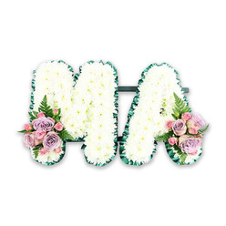 A beautifully composed sympathy tribute spells out the letters MA in full, standing side by side as a single, unified display on a pure white background. Both the M and the A are completely filled with dense white chrysanthemums, each flower head sitting snugly against the next to create a smooth, cushion-like surface that feels soft and comforting even at a distance. Around the outer edges, a rich green satin ribbon is expertly pleated and pinned in place, tracing every angle and curve so that the letters remain strong and clearly legible. This deep green outline adds definition and a touch of classic funeral elegance. Nestled at the bottom left of the M and the lower right foot of the A are two floral accents that bring gentle colour and emotion: clusters of lilac and pale pink roses, supported by tighter pink spray roses and sprigs of foliage, form rounded posies that lean slightly outward. A single fern frond in each cluster stretches gracefully beyond the petals, giving movement and a hint of garden freshness. The arrangement feels contemplative and loving, as if created to honour a mum, mama or special woman remembered with warmth on quiet Canonbury streets. The style is timeless and traditional, the sort of bespoke funeral lettering an experienced Canonbury florist would design for a church service, crematorium chapel, or private family farewell, offering visual comfort when words alone are not enough.