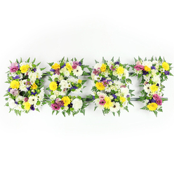Presented against a stark white backdrop, the floral letters spelling BEST feel both intimate and grand: four individual forms hewn from a rich meadow of carefully chosen blooms and greenery. Viewed head-on, each letter's face is a tapestry of texture - large, multi-petaled white chrysanthemum-like flowers create a soft, cloud-like base, while golden-yellow roses and sunflower-bright gerbera daisies introduce an uplifting warmth. Scattered throughout are clusters of mauve to deep purple lisianthus or petite chrysanthemums that lend quiet depth, and cheerful fuchsia-pink spray roses or carnations that add lively punctuation. The letters are rimmed with deep-green fern fronds whose lacy edges cradle the blooms and define the letter shapes with natural grace. A discreet dark green or metallic support bar peeks through in a few places, a testament to the careful handcrafting and structural thought behind the installation, particularly visible across the E's horizontal bar and the T's crosspiece. Even, bright lighting highlights the freshness - petals appear satiny, foliage looks glossy, and textures are sharply readable. There is an evocative scent memory in this arrangement: a soft mix of rose, green fern, and the earthy, faint spiciness of chrysanthemums. The overall impression is one of tender celebration and thoughtful remembrance; families in Canonbury and nearby De Beauvoir often choose similar lettering tributes for wake décor or to lay at a favourite spot in Canonbury Square Gardens, where the flowers can speak quietly of love and loss.