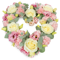A carefully crafted heart-shaped floral wreath rests against a pure white background, its generous size and fullness immediately catching the eye. The heart is built from a tapestry of soft, romantic colours, dominated by creamy ivory and pale yellow roses that form luminous focal points. Each rose is perfectly formed, with tightly layered petals that spiral inward, symbolising a quiet, enduring love. Between them, clusters of pastel pink carnations add a gentle, feathery texture, their frilled edges softening the heart's outline so it appears almost like a cushion of petals. Deeper rose-pink and mauve lisianthus blooms are scattered through the design, their slightly looser, trumpet-like petals creating pockets of depth and visual interest. Small yellow-green buds dot the arrangement, like tiny promises of new blossoms yet to open. Woven throughout are stems of cool, silvery eucalyptus, their rounded leaves providing a serene contrast to the pastel flowers and helping to shape the heart's curves with natural grace. There is a sense of calm, as if the flowers have been arranged in gentle daylight coming through a Canonbury townhouse window. The wreath feels like a comforting presence, ideal for a memorial service at a local chapel or a farewell gathering near Highbury Fields, where families come together to share memories. Every bloom appears freshly placed, suggesting same-day creation by a skilled Canonbury florist who understands how to express sympathy, remembrance, and love without words. This floral heart would be chosen when someone wants a tribute that is both elegant and profoundly personal.