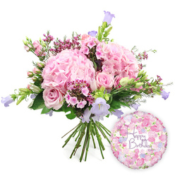 A lush birthday bouquet in pastel pinks and purples is captured in front of a pure white backdrop, offering the feel of a freshly prepared arrangement resting on a Canonbury workbench. The composition is dominated by several large, rounded heads of pale blush hydrangea, their countless petals packed closely together to create a soft, billowing texture, almost like folds of fabric. Nestled among these generous clusters are tender pink roses and spray roses, some beginning to unfurl into layered rosettes while others remain tightly cupped, offering a charming mix of openness and promise. Fine sprays of vivid fuchsia or magenta waxflowers run between the larger blooms, their tiny star-like flowers bringing a lively sparkle of colour and a sense of intricate craftsmanship. Taller threads of campanula, with their slender stems and bell-shaped flowers in cool lavender and light periwinkle, rise gently from within the bouquet, adding a subtle vertical lift and a hint of wildflower grace reminiscent of a walk through nearby Highbury Fields in spring. Fresh green foliage encircles and fills the bouquet, its variety of leaf shapes and tones creating depth and giving the hand-tied design a natural, garden-picked character. The stems are carefully gathered and cinched at the base, splaying slightly where they meet the clean white surface beneath. To the lower right sits a single round foil balloon, its metallic sheen catching the light. The balloon is decorated all over with delicate pink and lilac floral motifs and carries the message "Happy Birthday" in a decorative purple script, echoing the bouquet's palette and completing a joyful, ready-to-deliver birthday gift that would feel perfectly at home in any Canonbury townhouse or flat along St Paul's Road.