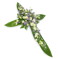 From a slight overhead perspective on a plain white backdrop, this elegant sympathy cross marries bold tropical foliage with a soft, restrained floral palette to create a composed, consoling tribute. The structure is built of wide, glossy green leaves - their smooth, almost waxy surfaces and distinct veins laid carefully to form the vertical and horizontal arms - giving the cross a verdant, sheltering base. At the intersection and reaching along each arm, clusters of creamy ivory and white lisianthus unfold with layered, ruffled petals; between them sit small, rounded white chrysanthemum-type blooms and tightly furled buds that add compact texture and luminous highlights. Interspersed through the white clusters are fine sprays of pale lavender limonium or aster, tiny star-shaped blossoms that introduce a whisper of purple and bring depth to the arrangement's centre. Slim sprigs of delicate green filler foliage are woven through the flowers, softening transitions and lending the piece a meadow-like intricacy. The light is soft and even, accentuating the sheen of the leaves and the silky translucence of the petals, while the composition reads as both composed and tender. As a local Canonbury florist I often recommend this design - crafted here at Canonbury Flowers - for church services along Essex Road or peaceful memorials near Canonbury Tower; it communicates reverence, quiet hope and enduring affection. The overall scent is subtle and green, the touch a contrast of waxy leaves and feather-soft petals, and the arrangement's classic cross silhouette makes it a respectful choice for funerals, wakes or religious tributes in the Islington neighbourhood.