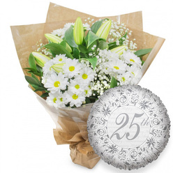 Set against a clean, uncluttered white backdrop, this image shows a refined anniversary bouquet and a matching silver balloon that capture the dignity and joy of a 25th celebration in Canonbury. The bouquet is dominated by fresh white chrysanthemums, their daisy-like petals forming perfect circles around warm yellow centers that bring a touch of sunshine to the arrangement. Rising through the cushion of daisies are several long, elegant white lily buds, some tightly closed and others just beginning to loosen at the tips, their subtle green undertones hinting at the fullness of bloom still to come. Between these larger flowers, fine sprays of white baby's breath thread delicately through the design, like a soft mist, giving depth and a romantic texture. Deep green foliage fans out behind and below the flowers, the leaves sturdy and full, creating a vivid contrast that makes every white petal stand out. The bouquet is wrapped first in clear, protective cellophane and then enveloped in natural brown kraft paper that has a slightly rustic, market-fresh feel, as though just collected from a local stall near Canonbury Station or along Upper Street. The stems are neatly bound at the base, suggesting a bouquet prepared for easy gifting and home display. To the right of the flowers, a gently gleaming silver foil balloon adds to the sense of occasion. Its round face is decorated with ornate scrollwork in a deeper shade of silver, and at its center the inscription "25th" appears in an elegant script, surrounded by faint repetitions of "Happy Anniversary." The metallic surface is minutely crinkled, catching the light in small highlights that echo the bouquet's quiet sparkle, making this pairing perfect for honouring a silver wedding anniversary or a quarter-century milestone in North London.