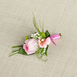 Gracefully nestled on a subtly textured linen reminiscent of the artisan fabrics found at Canonbury's local markets, this boutonniere tells a story of romantic celebration. Its centrepiece, a gently blushing pink rose, holds onto its freshness in a tightly furled spiral, the petals blending from vibrant deep pink at the core to the lightest pastel at the tips-evoking the early blossoms of springtime in nearby Highbury Fields. Alongside this, a delicate peach-toned flower, likely an alstroemeria, unfurls its petals to reveal touches of golden yellow and intricate dusk-brown flecks, adding personality and visual intrigue. Wispy sprigs of baby's breath and compact green cushion mums mingle with spiky dark grass blades and soft, folded leaves, their vibrant hues made richer by the sunlight that filters across the grains of fabric. At the base, a bold and glossy fuchsia satin ribbon is expertly wound and tied, reflecting both joy and a sense of celebration with its glimmering bow. The skill of Canonbury Flowers' florists is evident in every precise detail-from the interplay of colours to the tactile contrasts of soft petals and crisp greenery. This arrangement feels perfectly at home at a wedding on Compton Terrace, a christening in Newington Green, or any event that celebrates life's big moments. Each element is thoughtfully placed, creating a visual story that resonates with Canonbury's calm sophistication and timeless charm.