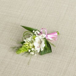 On a pale, linen-like fabric background the colour of warm sand, a compact floral boutonniere has been carefully laid out as if waiting on a suit jacket in a Canonbury townhouse. The central flower is a white alstroemeria, fully open, its petals silky but slightly papery at the tips, each one marked near the centre with fine reddish-brown flecks that draw the gaze inward to the delicate stamens. Flanking it is a bright lime-green spike of tightly packed buds, almost architectural in form, each bud forming a tiny scale that creates a ridged, conical silhouette and a vivid contrast to the smooth lily petals. Threaded between these structural pieces are airy stems of baby's breath, their clusters of minute white flowers giving an impression of floating snowflakes or early morning mist. The florist has built the base with a mix of glossy, dark green, lance-shaped leaves and finer, grass-like fronds that curl and sweep, adding depth and a sense of gentle movement as they fan out beneath the bloom. The stems are gathered and secured with a slim satin ribbon in bright pink, tied into a crisp, symmetrical bow whose soft sheen catches the light and introduces a joyful, romantic note. The scene is evenly lit, revealing the freshness of every element, from the cool whiteness of the petals to the lively greens of the foliage. The overall mood is calm, pure, and quietly celebratory, perfectly suited to a wedding morning in Canonbury, perhaps for a ceremony just off Essex Road or a reception near the leafy paths of Highbury & Islington, where subtle details matter as much as grand gestures.