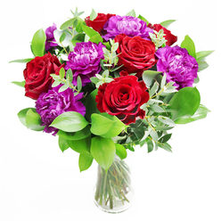 In this elegant arrangement, imagined on a polished table in a Canonbury living room, deep red roses and vivid purple peonies create a striking duet of colour and texture. The roses are at that perfect stage of bloom where each flower has fully opened but still holds its shape, petals curling outward in soft, velvety spirals, the red so intense it seems to radiate warmth. Interwoven among them, the purple peonies offer a different kind of drama: their blossoms are round, full, and gently ruffled, layers upon layers of petals giving a sense of abundance and quiet luxury. A generous layer of greenery forms a supportive cradle, with mixed foliage in varied shades of green providing contrast and freshness. Some leaves are smooth and glossy, reflecting the light, while others are more matte and feathery, creating a soft halo around the central blooms. Slender stems of eucalyptus arch through the bouquet, their cool, silvery-green discs introducing a contemporary twist and a subtle, refreshing scent. All of this sits in a simple, clear glass vase, the clean lines allowing the stems to be seen as they gather and cross, adding an understated, natural structure. The light appears to fall from one side, as if from a nearby Canonbury café window, casting gentle shadows and making the reds and purples glow. This bouquet feels ideal for celebrating a promotion, marking an anniversary dinner near Upper Street, or sending an exuberant message of admiration, the kind of floral gift crafted with care that speaks as much through its artistry as through its fragrant, colourful presence.