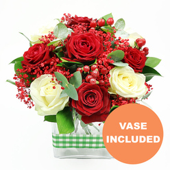 Against a crisp white backdrop, a carefully composed bouquet of red and white roses draws the eye with its rich colour and gentle symmetry, as though it has just been set down on a polished table in a Canonbury terrace. Full, velvety red roses are interlaced with creamy white blooms, each rose perfectly unfurled so the layered petals form soft spirals of light and shadow. Between them, tiny scarlet filler flowers resembling dyed baby's breath create a misty, textured layer, their small blossoms lending a sense of delicacy and intricacy to the design. Clusters of round, glossy red hypericum berries sit like bright beads among the petals, their shine adding a festive sparkle that feels at home during winter celebrations or romantic evenings along Upper Street. The arrangement is threaded with fresh greenery, including sprigs of silvery eucalyptus and other lush green foliage, which offers contrast to the rich reds and creams while suggesting a clean, herbal freshness. All of the blooms and leaves are gathered in a sleek, clear rectangular glass vase, allowing the neat stems to be seen and grounding the bouquet in a contemporary style that suits modern Canonbury apartments and classic period homes alike. Around the middle of the vase, a green and white gingham ribbon is snugly tied, introducing a touch of rustic charm that recalls local farmers' market stalls. In the lower right-hand corner, an orange circular graphic with the words VASE INCLUDED in white stands out clearly, signalling that this thoughtfully arranged floral gift arrives complete and ready to place as a centrepiece for anniversaries, birthdays, or quiet at-home celebrations.