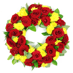 A meticulously crafted circular funeral wreath, rich with deep red roses and bright yellow chrysanthemums, is shown in sharp detail against a simple white backdrop, as if resting on the counter of a Canonbury florist just off Essex Road. The wreath forms an unbroken ring with a clear open centre, its symmetry and density revealing hours of careful work. Red roses, in full bloom, are the stars of the piece: their petals curl outward in neat spirals, layering from a classic crimson core to velvety, darker edges that almost lean towards burgundy. Tucked thoughtfully between these roses are generous clusters of sunny yellow chrysanthemums, their many fine, thread-like petals creating little bursts of light and texture that soften the design. Surrounding and weaving through the flowers is a base of fresh green foliage, likely a mix of glossy salal and softer, misty-green eucalyptus. Some leaves catch the light with a faint sheen, while others appear more matte, giving the wreath a gentle, natural variation that feels like a walk through nearby Highbury Fields. The foliage supports the blooms without overwhelming them, helping the circle stay full and rounded from every angle. Bright, even lighting highlights the contrast between the intense reds, cheerful yellows, and cool greens, while the white background keeps the focus firmly on the tribute itself. The overall mood is one of calm respect and heartfelt emotion, well suited to a funeral or memorial service in Canonbury, where family and friends might gather to remember a loved one with a floral tribute that speaks quietly of love, comfort, and enduring connection.