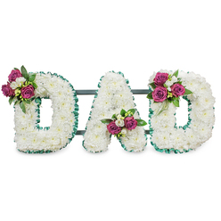 This striking sympathy arrangement spells out "DAD" in bold, capital letters formed from hundreds of immaculate white chrysanthemums or comparable soft white florets, each bloom nested so closely the letters take on a plush, three-dimensional presence. The white surface feels serene and pure beneath a gentle, even light, its textural softness evoking quiet reflection. Each letter is carefully edged with an emerald green pleated ribbon, the ruffled trim following the outer and inner contours to create a crisp silhouette against the white field. A subtle dark green or slate-grey horizontal bar runs behind the letters, unobtrusive yet clearly supporting the display for placement at a wake, chapel or graveside. Artfully positioned accent clusters bring warmth and colour: rich magenta-pink roses in varied stages of bloom-some tightly furled, others opening-are set on the upper left curve of the first "D", nestled into the lower V of the "A", and mirrored on the upper right curve of the final "D". Sprays of delicate white freesia or similar small blooms add a gentle perfume and a lighter texture among the roses, while deep green foliage provides contrast and weight. As a local florist might describe it, this composition balances traditional reverence with personal tenderness; you can imagine it arranged for a funeral service near Essex Road or laid as a graveside tribute at a nearby cemetery, communicating love, remembrance and a composed farewell.