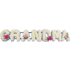A beautifully composed funeral flower tribute spells out "GRANDMA" in bold, cushiony letters, each one fully dressed in tightly clustered white chrysanthemums that create a dense, pillowy surface. The petals form a soft, rippling texture, evoking the comforting feel of a grandmother's warm embrace. Around the outer edge of every letter, a narrow lilac ribbon is carefully pinned in place, its pastel tone adding refinement and a calm, respectful frame to the crisp white flowers. Three focal points bring gentle colour into the arrangement: at the lower curve of the "G", across the central "A", and at the final "A", small hand-tied posies of pink gerberas and delicate pink roses appear, accented with feathery greenery. These accents look like tiny garden moments tucked into the more formal lettering, suggesting bright memories within a peaceful farewell. Soft, diffused light washes over the display, highlighting the natural sheen of each chrysanthemum petal and the velvety texture of the roses, while the lilac edges catch the eye without overwhelming the design. It feels like the sort of heartfelt tribute families in Canonbury might choose when saying goodbye at a local service, perhaps after a quiet walk through nearby New River Path or around Canonbury Square. Crafted with evident care and precision, the arrangement balances sorrow and gratitude, offering a gentle message of love and remembrance for a cherished grandmother whose presence shaped the everyday life of her family.