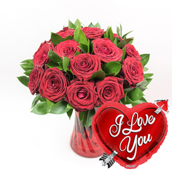 A lavish bouquet of red roses fills the scene with the intensity of a heartfelt "I love you," carefully arranged as though by an experienced Canonbury florist preparing a special delivery for a nearby townhouse. At the centre, a generous cluster of deep crimson roses rises from a ruby-red glass vase, each bloom heavy with velvety petals. Some roses are fully open, showing spiralled hearts and soft, layered edges, while others remain in that perfect in-between stage-partly unfurled, promising days of beauty to come. Around them, rich green foliage, polished and fresh, creates a frame that makes the red tones glow even more vividly, like a patch of colour against the calm architecture of Canonbury's quiet streets. The vase itself is clear but tinted a luscious ruby hue, with graceful, fluted ridges that draw the eye down to where the stems gather in the water. The light glints along the glass, echoing the shimmer of the metallic details nearby. In the lower right corner of the composition, a heart-shaped red foil balloon nestles close to the arrangement, its surface glossy and reflective. Across its centre, the phrase "I Love You" is written in sweeping white script, and an elegant silver Cupid's arrow appears to pierce the heart at a diagonal. Against the simple white background, the reds and greens stand out with striking clarity, giving the whole image a clean, modern feel while still being unabashedly romantic. It's the visual essence of a grand romantic gesture, ideal for anniversaries, Valentine's Day, or any day when words alone feel too small.