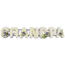 The image shows a carefully composed floral lettering tribute spelling GRANDPA in large, sculpted capitals, presented horizontally as though ready to be placed beside a coffin or at the front of a chapel in Canonbury. Each letter is fully carpeted with tightly packed white chrysanthemums or carnations, every floret facing outward to form a smooth, cushioned surface with a soft, velvety texture. The whiteness feels calm and steady rather than stark, evoking respect, gratitude, and the quiet love often felt for a grandparent who has guided the family over many years. Nestled within this sea of white are thoughtful accents of rich purple and lavender blooms, possibly lisianthus or small irises, arranged in modest clusters with fresh green foliage that peeks through. These touches appear in the rounded bowl of the G, inside the open triangles of the As, and across the curves of the D and P, adding depth and a gentle rhythm of colour, like small moments of shared memory amid grief. A dark green frame or bar runs just beneath the letters, largely concealed by the flowers yet providing essential structure so the word stays perfectly aligned when transported to a service in nearby Barnsbury, De Beauvoir, or along Essex Road. The tribute feels both strong and tender, a bespoke sympathy arrangement that could be ordered for same-day delivery across Canonbury to honour a cherished grandfather, offering a focal point of remembrance and a place for the family's eyes to rest during the sadness of a funeral or memorial gathering.