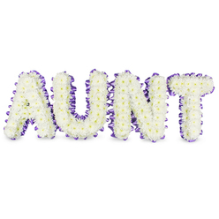 This handcrafted floral letter tribute spells 'AUNT' in bold uppercase, each character densely formed from hundreds of pristine white spray chrysanthemums whose tiny petals overlap to create a soft, cloud-like texture. Small, pale yellow centres appear within the blooms like faint suns, lending warmth amid the cool white canvas. A rich purple satin ribbon, neatly ruched and slightly pleated, frames the edge of every letter; its satin sheen and deep hue set off the flowers and give the composition a refined, finished look. The letters cast delicate grey shadows on the white backing, reinforcing their three-dimensional structure and making the message read with clarity and presence from across a room. The aroma is gentle and green - fresh chrysanthemums with a dewy undertone - an unobtrusive comfort at a funeral or memorial.  Created by Canonbury Flowers with the sensitivity of an Islington-based florist who knows the neighbourhood's pace, this tribute is designed to be both personal and enduring. I often imagine it placed near Canonbury Square or delivered to services on Essex Road, offering attendees a focal point for memories and quiet reflection. The white and purple palette feels both respectful and quietly celebratory, a dignified nod to a life well loved. As a bespoke memorial piece, it communicates care and attention to detail, helping families express their affection and honour a beloved aunt in a setting that matters to them.