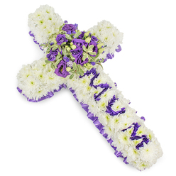 A carefully crafted Christian cross made from countless small white chrysanthemums, each bloom arranged closely to form a plush, cushion-like surface that reads as peaceful and reverent. The outer edge of the cross is traced with a ruffled satin ribbon in a deep purple hue, the pleating catching the light and lending a refined, solemn border. Prominently down the vertical stem the letters "MUM" are spelled in compact purple blooms - likely eustoma (lisianthus) or small spray chrysanthemums - the rich violet tone creating a heartfelt, readable dedication against the pristine white base. At the crossroads of the arms sits a generous central spray composed of deep violet roses paired with lighter lavender lisianthus, their contrasting petal shapes and tones producing a focused, contemplative centrepiece. Variegated foliage, perhaps pittosporum or a similar leaf with pale margins and darker centres, frames the blooms and introduces a crisp, natural texture, while small green berries add a discreet tactile accent. Photographed against a stark white background, the overall palette of pure white and layered purples suggests a message of respect, dignity, and comfort. The bouquet's textures - from the chrysanthemum's soft density to the roses' velvety spirals and the ribbon's satin sheen - invite a gentle touch and quiet reflection. As a local florist serving Canonbury and nearby Upper Street and Essex Road funeral venues, Canonbury Flowers prepares this style for sympathetic deliveries and memorial services, mindful of both craftsmanship and the emotional need for a dignified farewell.