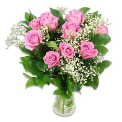 A rounded bouquet of pink roses and white baby's breath is presented in a simple clear glass vase, set against a bright white background that makes every detail stand out with calm clarity. Around a dozen roses in shades of soft shell-pink to medium, candy-floss pink cluster closely together, some fully open with layered, cupped petals, others just beginning to unfurl like tiny promises. Between the roses, delicate sprays of white baby's breath form a fine, cloud-like veil, their miniature blooms lending a sense of airiness and innocence that feels especially fitting for celebrating a new arrival. Glossy, dark green foliage surrounds the flowers, its slightly serrated edges and natural sheen evoking the feel of a freshly gathered garden bunch, as if it had been cut that morning from a hidden plot off Canonbury Square. The vase itself is unadorned, allowing the stems-pale green and neatly trimmed-to be seen through the clear water, suggesting careful conditioning by an experienced florist. Gentle, even lighting smooths across the arrangement, creating soft highlights on the roses' velvety surfaces and subtle shadows that add depth without drama. The bouquet's overall impression is one of quiet joy and warmth, making it a beautiful choice for baby flower deliveries across Canonbury, Highbury, and nearby Islington streets. It would sit effortlessly on a bedside table in a maternity room or on a windowsill in a nursery, offering a graceful, soothing burst of colour as family and friends celebrate a new chapter in life.