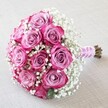 Arranged with precision and affection by Canonbury Flowers, this enchanting round bouquet is a feast for both the senses and soul. Around a dozen two-tone pink roses, with centers of soft lavender-pink fading to rich magenta at the edges, form a lush, domed focal point reminiscent of blooms found in Arlington Square Park. Airy clusters of white baby's breath interlace the arrangement, providing gentle contrast and capturing light with their delicacy. The hand-tied stems are wrapped with a silky, blush-pink ribbon that gleams softly-accented by a spiral of petite, lustrous pearls, paying tribute to Canonbury's refined ambiance. The natural ends of the stems peek from beneath the wrap, signaling unmatched freshness and the artisan care of a local florist. All set atop a lightly textured, off-white fabric reminiscent of sunlit wedding linens, the bouquet glows beneath diffused, natural daylight. Each petal, sprig, and pearl is highlighted, celebrating skilled craftsmanship and emotional resonance. Whether chosen for a wedding ceremony in Canonbury or as a romantic anniversary gift, this bouquet evokes love, happiness, and the enduring beauty of life's most cherished moments-all reflected in the surroundings and spirit of Canonbury.