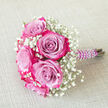 Set against a neutral, woven beige fabric that looks like softly lit linen, this compact bouquet radiates poised, romantic charm, as if prepared in a quiet Canonbury studio minutes before delivery. The focal point is a cluster of lush bi-colour roses, each bloom unfurling from a cool, misty lavender or lilac centre into dramatically darker fuchsia and magenta-pink edges. The petals layer in tight spirals, velvety and almost luminous, creating a striking ombré effect that feels both modern and timeless. Around and between these statement roses, airy sprays of white baby's breath drift like tiny clouds, their countless miniature blossoms adding a whisper-light texture and a sense of purity. The stems are expertly bound in a deep purple satin ribbon that hugs the handle smoothly, its sheen suggesting careful, practiced hands at work. Over this, a string of luminous white faux pearls curls in a deliberate spiral, reminiscent of a favourite necklace tucked away in a Canonbury terrace bedroom and brought out for special occasions. The bouquet is positioned diagonally with its pearl-trimmed handle leading the eye to the right edge of the image, giving the impression it has been gently placed down between photographs at a local Islington registry office or just before a garden ceremony near New River Walk. The mood is tender yet confident, ideal for a bridesmaid, prom guest, or anyone marking a cherished milestone with flowers that feel personal, handcrafted, and freshly arranged for a memorable day.