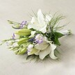 Lying serenely on a natural, soft beige linen backdrop, this luxurious floral bouquet exudes the sophistication and quiet joy that Canonbury is known for. Dominated by impressive white Oriental lilies-some blooms fully unfurled, others delicately opening-each flower's broad petals are perfectly pure, framing a golden cluster of anthers at the throat. Scattered throughout are the enchanting, two-toned lisianthus flowers; their white petals are edged with deep purple, evoking twilight blooms in a Canonbury garden. Emerging buds add a layer of promise and tenderness. Vertical accents of slender purple Veronica weave deeper shades into the look, while tiny, cloud-like sprays of baby's breath interlace with softly arching, feathery fern. The fresh, abundant green foliage encircles the bouquet, its textures echoing the leafy escapes of New River Walk. Tightly gathered stems, bound with an understated white ribbon, ensure the bouquet's hand-crafted charm and bring a touch of local artistry from Canonbury Flowers. Under diffused light, every curve and hue radiates, casting subtle shadows for a gentle depth. Perfect for a bride's special day, a radiant anniversary, or as a centerpiece to brighten an Islington townhouse, this arrangement captures the poetic essence of Canonbury in every bloom.