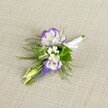 A finely detailed close-up of a wedding boutonniere rests on softly textured light beige linen, the neutral fabric catching gentle, natural light and giving the flowers a calm, elegant stage. At the heart of the buttonhole are two fully opened lisianthus blooms, their petals a creamy white that gradually shifts to a rich, velvety purple along the ruffled edges, as if each petal has been hand-painted. Just beside them, a slim vertical spike of muscari rises, made up of tiny, tightly packed, bell-shaped flowers in a deep grape-purple tone, adding an interesting, architectural line to the design. Around these focal flowers, delicate clusters of tiny white filler blossoms, reminiscent of baby's breath, drift like soft clouds, lending a light, airy feel. Fine, feathery greenery, similar to asparagus fern, fans out in gentle sprays, bringing a fresh meadow-like texture that contrasts beautifully with the more structured blooms. Two pale green, unopened buds nestle within the arrangement, suggesting new beginnings and quiet anticipation. The stems are neatly gathered and wrapped in crisp white satin ribbon, smoothed flat and finished with a small, tailored bow that signals the piece is ready to be pinned to a lapel. The overall mood is refined yet romantic, like something a groom might wear for a Canonbury ceremony near the leafy edges of Highbury Fields, or a prom guest meeting friends along Islington's quieter side streets. The image captures not only the colours and shapes but the sense of a treasured, thoughtful floral detail prepared by a local florist with an eye for understated sophistication and timeless style.