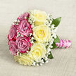 Placed gently on a pale, woven fabric that looks like fine linen or hessian in soft oatmeal and cream tones, this classic hand-tied bouquet is captured from above so its full, circular form can be admired. The arrangement is thoughtfully divided into two distinct halves: one side is a sumptuous sweep of vivid fuchsia and magenta-pink roses, their petals layered in plush spirals, each bloom at perfect, open maturity; the other half overflows with creamy, light yellow roses, their buttery centres fading to softer ivory at the tips. Together, the colours echo a summer sky over Canonbury's leafy streets-warm, cheerful, and quietly sophisticated. Interlaced throughout the bouquet, delicate sprays of white baby's breath float between the larger flowers, like tiny stars in a pastel dusk, lending an ethereal, traditional bridal touch. Here and there, deep green leaves emerge from the mass of petals, offering contrast and a sense of garden freshness that feels at home near Canonbury's hidden courtyards and landscaped terraces. The stems are neatly trimmed and bound into a comfortable, hand-held shape, carefully wrapped in glossy pink satin ribbon. Around this, a single strand of white pearls winds in a graceful spiral, reminiscent of a cherished necklace worn on a wedding day, adding refinement and a subtle hint of luxury. The gentle, neutral background allows the bouquet's colours and textures to take centre stage, inviting you to imagine the soft fragrance of the roses and the rustle of satin as the bouquet is carried down the aisle in a Canonbury townhouse ceremony or an intimate local registry wedding.