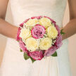 A domed bridal bouquet glows softly in natural light, its creamy white and blush-pink roses gathered in a harmonious, rounded shape that sits neatly in the bride's hands. The ivory roses appear luminous and serene, their petals unfurling in generous layers, while the blush and soft magenta roses seem gently lit from within, like petals touched by the first light over Canonbury's quiet terraces. Delicate sprigs of baby's breath are threaded throughout the arrangement, adding a fine, lace-like texture that softens the transitions between each bloom and introduces a subtle haze of pure white. The bouquet feels expertly balanced: not too large, not too compact, its symmetry giving it a graceful presence against a lace or satin gown. Hints of deep green foliage, tucked low at the base, frame the flowers without drawing attention away from the roses' romantic colour palette. Imagine holding it while stepping from a townhouse near Canonbury Square to a waiting car, the scent of gently sweet roses drifting up like a private promise, evoking a garden at the height of spring. The petals would feel cool and silky on your fingertips, each bloom strong enough to last through a day of celebration yet delicate in appearance. This bouquet captures the tender excitement of a wedding day in Canonbury, quietly echoing the purity, optimism, and intimate charm of a local ceremony shared with close family and friends.