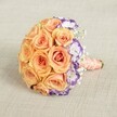 Presented against a soft, neutral fabric backdrop evocative of Canonbury's elegant interiors, this vibrant round bouquet is crafted with a lush mass of full-bloom peach and apricot roses. Their petals, rich and inviting, effortlessly form the domed heart of the design. Along one curve, a bold contrast emerges as white lisianthus with purple-brushed edges introduce a cool harmony and visual intrigue, conjuring the lively mix of tradition and creativity that defines Canonbury high streets. Wispy sprigs of white baby's breath dot the arrangement, particularly around the perimeter and interspersed among the roses, bestowing a dreamlike, airy glow. The bouquet's stems are tightly bound in smooth peach satin ribbon, culminating in a handle elegantly accented by a winding strand of lustrous cream pearls-ready for a bride's hand or as a gift for a milestone celebration. This arrangement radiates romance, sophistication, and a gentle connection to Canonbury's local charm, making it ideal for wedding parties, joyful anniversaries, or features on trending London floral styles.