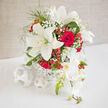 An elegant wedding bouquet brimming with ivory lilies and red roses is presented in a white woven container, its rounded form poised like a centerpiece on a softly lit Canonbury dining table. The lilies stand tall with star-shaped, creamy petals that open generously, each one edged with a subtle green tint that evokes freshness, as if the blooms were just delivered from a nearby London flower market. Between them, classic red roses fold layer upon layer of velvety petals, their rich, wine-toned centres suggesting romance, devotion, and the steady warmth of long relationships. Threaded through the composition, airy clouds of baby's breath bring a light, misty texture, gently bridging the visual gap between the stark white lilies and the passionate reds, much like how Canonbury's quiet side streets soften the bustle of nearby Upper Street. Small bunches of polished red berries punctuate the bouquet with cheerful brightness, echoing the joyful clink of glasses at an intimate reception in a local restaurant. The white woven vessel grounds the arrangement with understated sophistication, its subtle texture adding interest without stealing focus from the flowers it supports. A mix of fresh greenery peeks through the blooms, adding depth and framing the central blossoms so they appear both lush and effortlessly relaxed. The bouquet feels designed for a moment of significance-a wedding breakfast in a townhouse off Essex Road or a vow renewal overlooking a garden-where emotion runs deep but the style remains refined and timeless. Every angle reveals the careful work of an experienced Canonbury florist, who knows how to balance tradition with modern taste, creating a piece that feels both beautifully local and enduringly romantic.